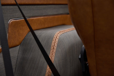 Close-up of rear seat fabric and tan leather trim with black seatbelt inside vehicle