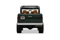 Rear view of Classic Ford Bronco with dark green body and tan seats, open top and roll cage