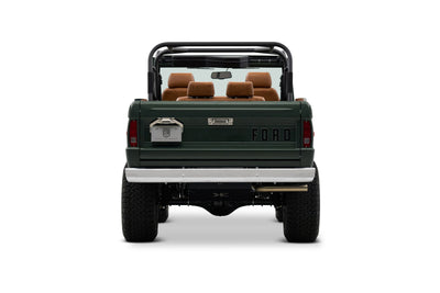 Rear view of Classic Ford Bronco with dark green body and tan seats, open top and roll cage