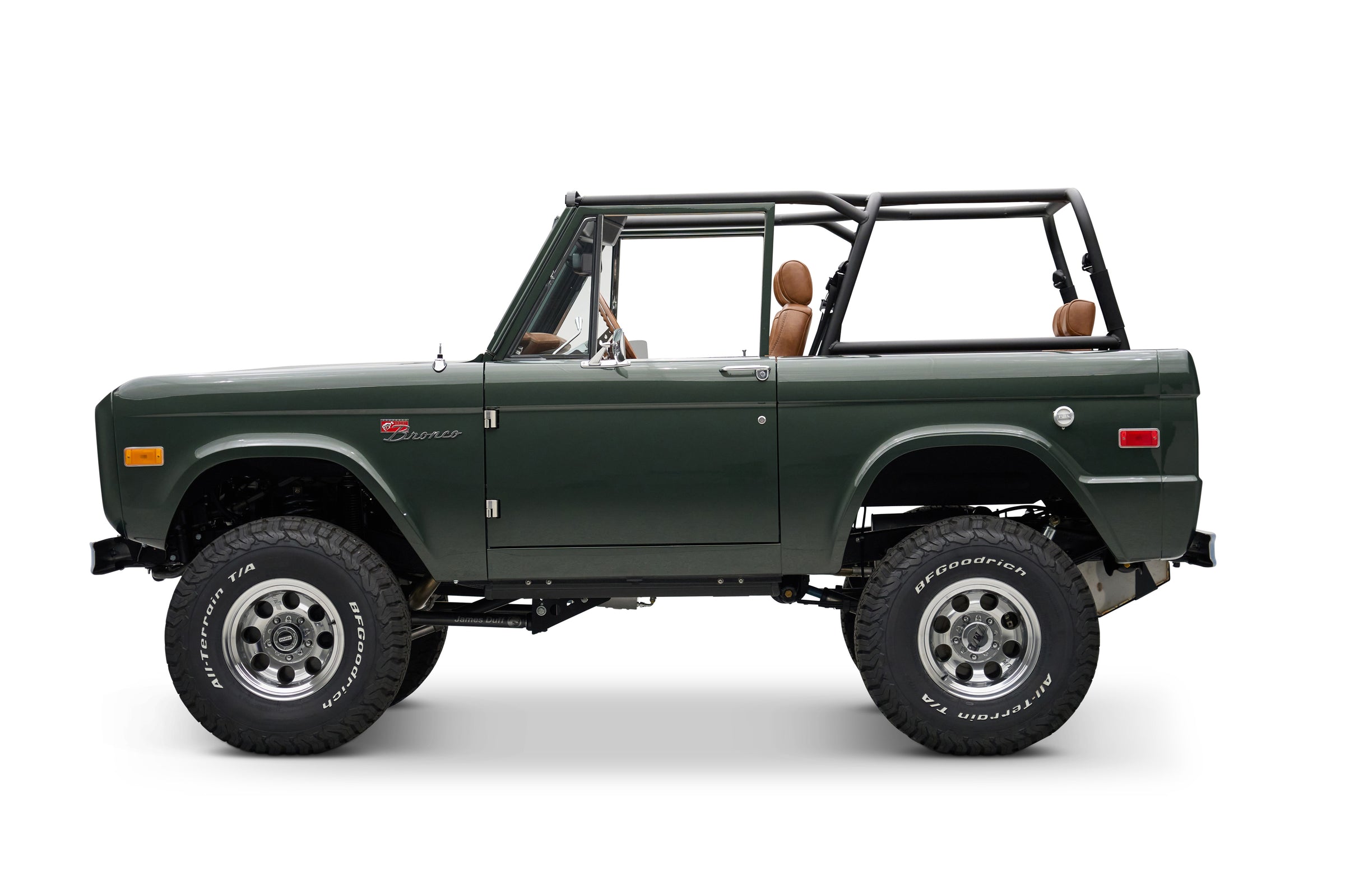 Side view of Classic Ford Bronco in dark green with tan seats, open top and large off-road tires