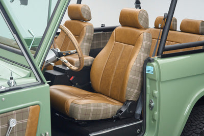 Interior front seats of Classic Ford Bronco with tan leather and plaid fabric, visible roll cage