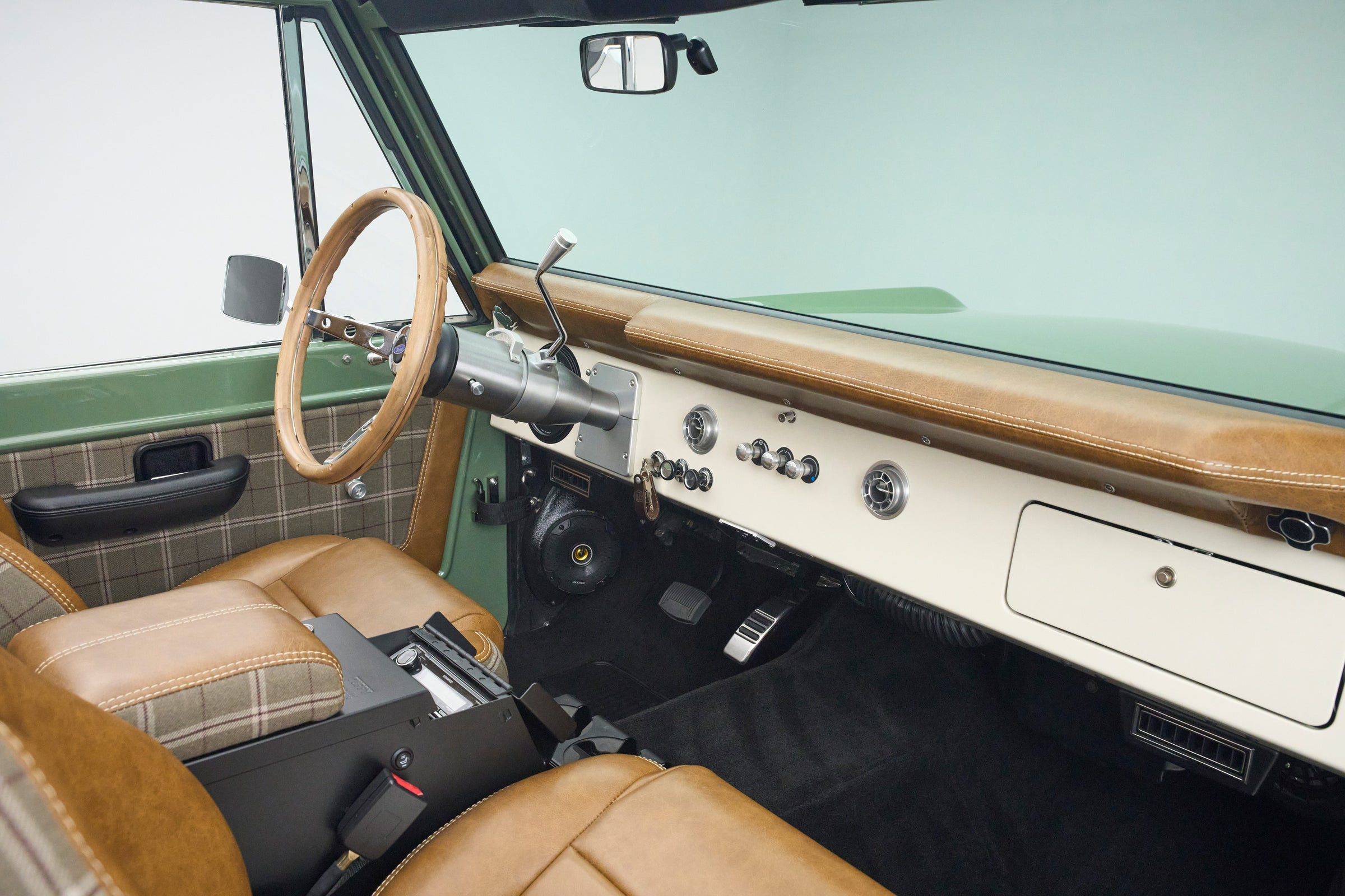 Classic Ford Bronco open door showing dashboard, steering wheel, and plaid leather front seats