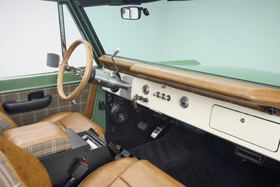 Classic Ford Bronco open door showing dashboard, steering wheel, and plaid leather front seats