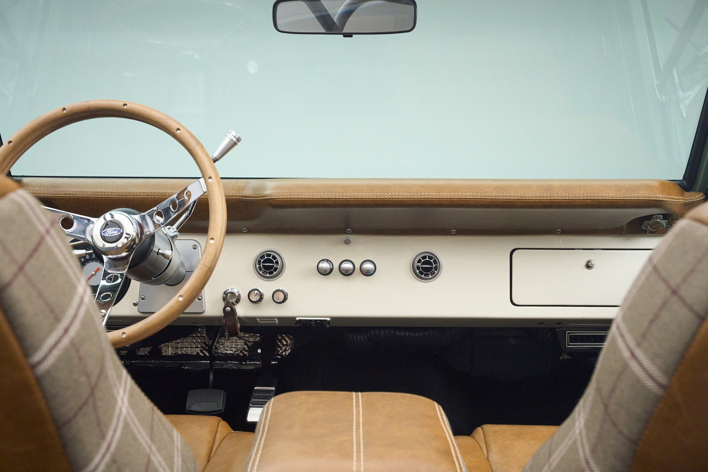 Interior view of Classic Ford Bronco dashboard with wood steering wheel and tan leather plaid seats