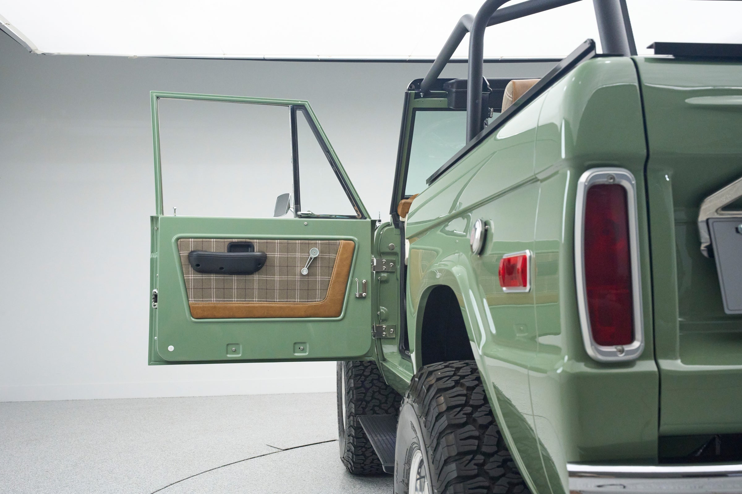 Open driver's door of green Classic Ford Bronco showing plaid and brown interior door panel