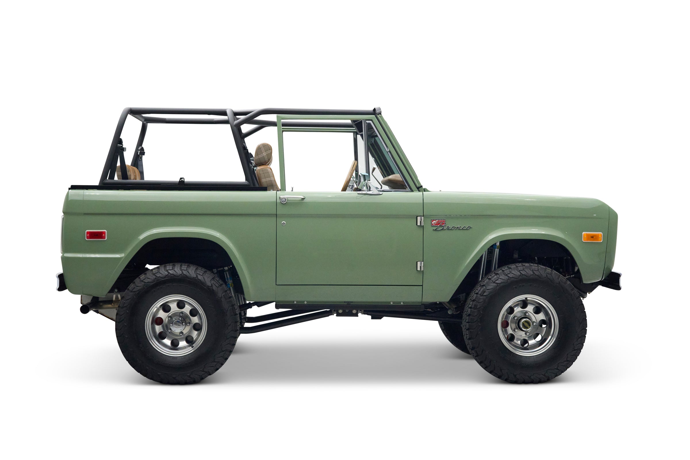 Side view of a green Classic Ford Bronco with black roll cage and plaid seats