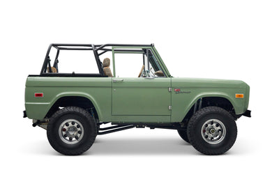 Side view of a green Classic Ford Bronco with black roll cage and plaid seats