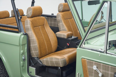 Front seats with brown leather and plaid upholstery inside green Classic Ford Bronco The Sutton