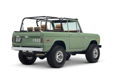 Rear three-quarter view of a green Classic Ford Bronco with open driver's door and black roll cage