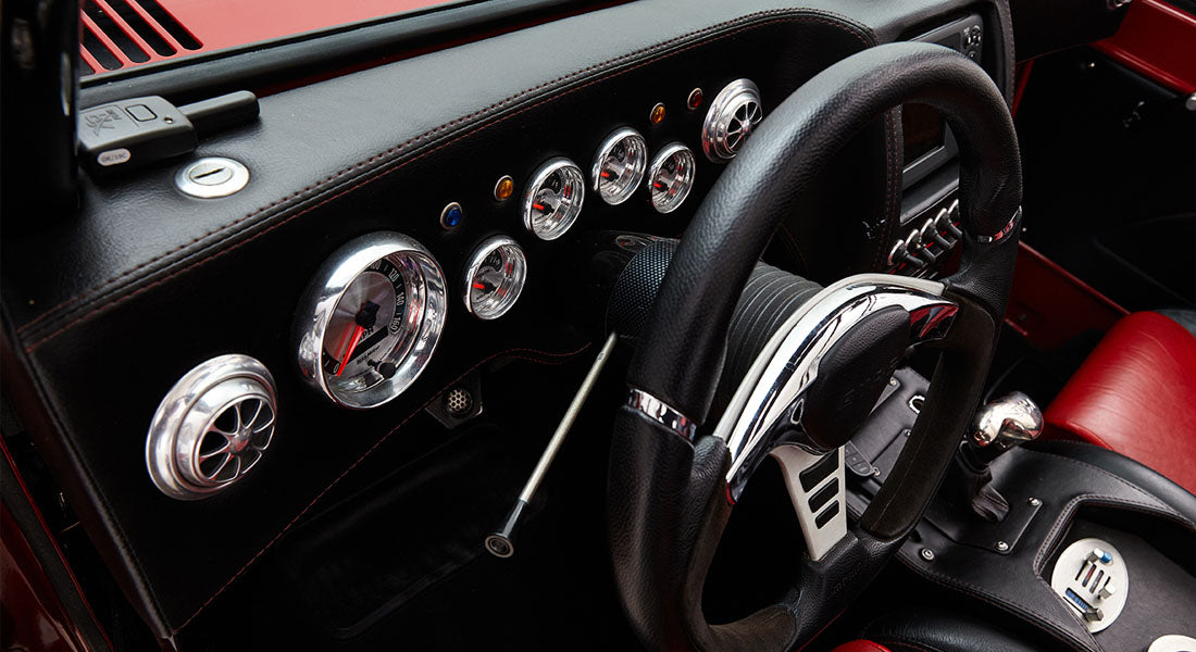Driver cockpit interior of Classic Ford Bronco showing steering wheel, gauges, and red interior accents.