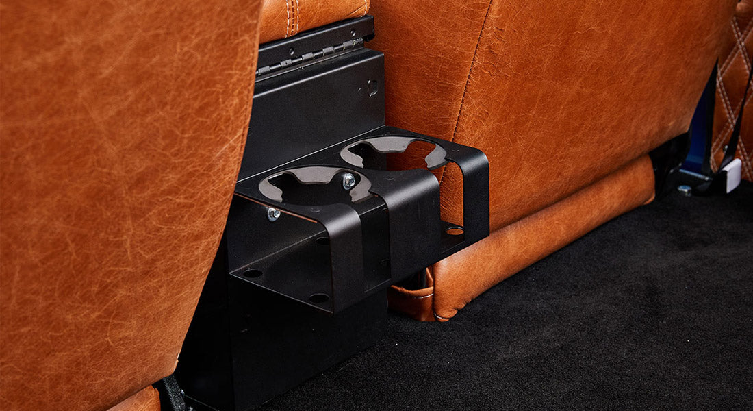 Two black metal cupholders mounted between brown leather seats inside a Classic Ford Bronco.