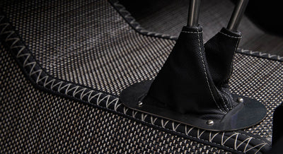 Black leather shifter boots on woven carpet with white stitching in vehicle interior