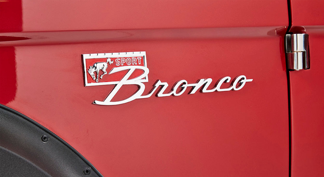 Red Classic Ford Bronco exterior showing chrome Bronco emblem and door hinge
