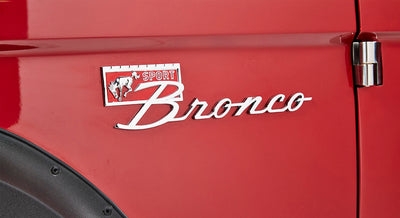 Red Classic Ford Bronco exterior showing chrome Bronco emblem and door hinge