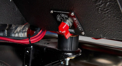 Red battery switch mounted on a black panel with wiring visible