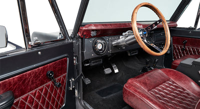 Interior driver cabin of Classic Ford Bronco showing red leather seats, dashboard, wooden steering wheel, and gear sticks.