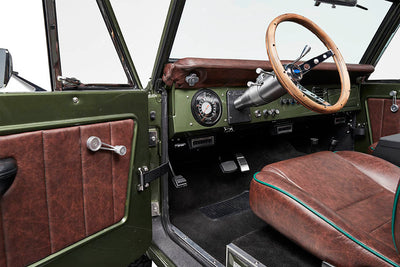 Open green Classic Ford Bronco door showing brown leather panel and wood steering wheel