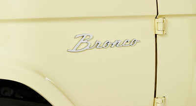Yellow Classic Ford Bronco exterior with chrome Bronco emblem and door hinge