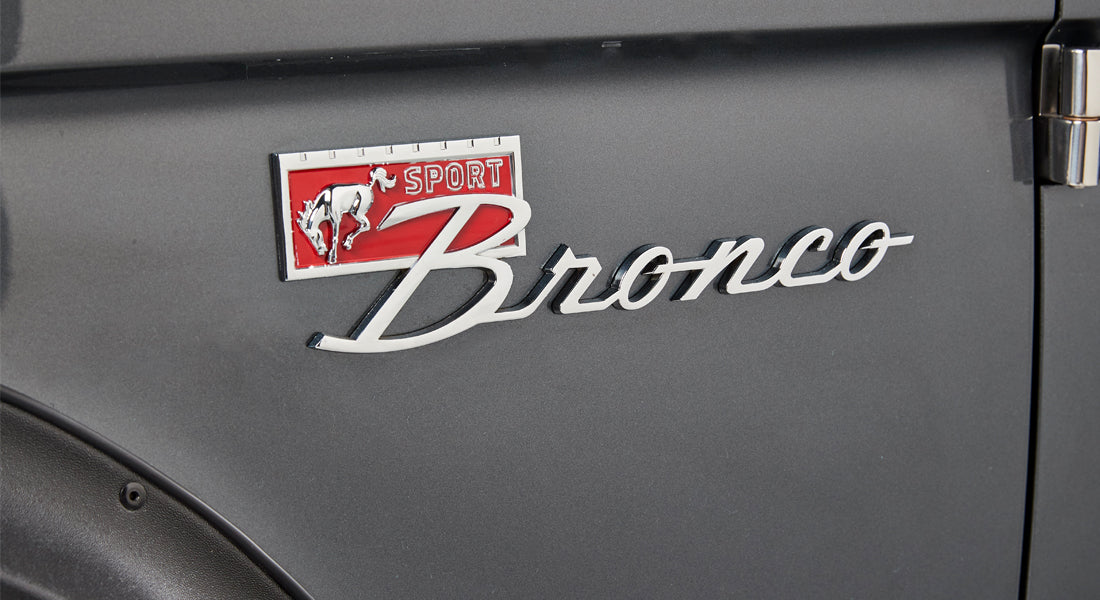 Close-up of a Classic Ford Bronco metal emblem with a running horse and red background on gray paint.