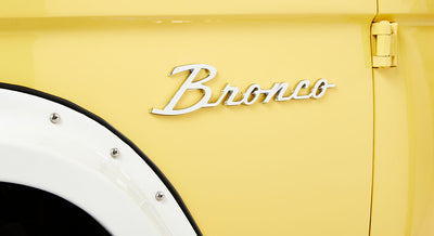 Yellow Classic Ford Bronco exterior close-up of chrome 'Bronco' emblem by the fender flare