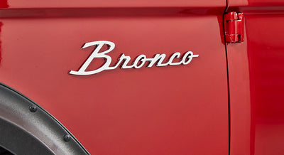 Red Classic Ford Bronco exterior showing chrome 'Bronco' emblem near the rear door hinge