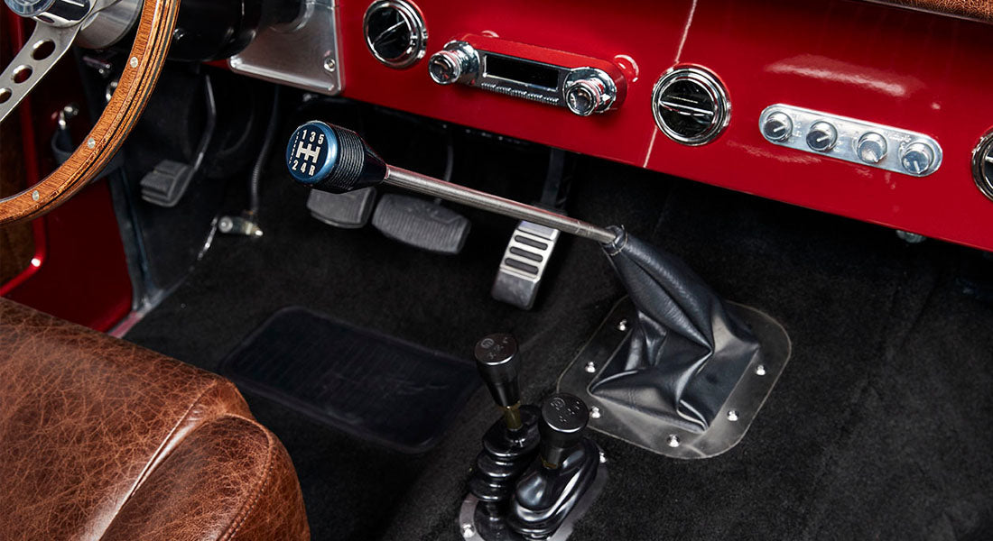 Classic Ford Bronco interior showing manual shifter, pedals, and part of red dashboard