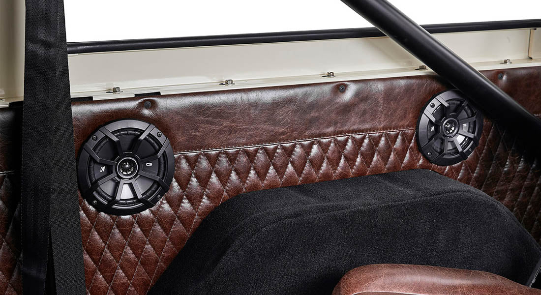 Two black round speakers embedded in brown diamond-stitched upholstery inside Classic Ford Bronco
