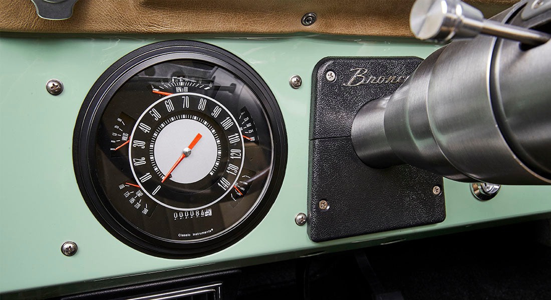 Classic Ford Bronco dashboard showing a large round speedometer and RPM gauge with Bronco emblem.