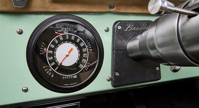 Classic Ford Bronco dashboard showing a large round speedometer and RPM gauge with Bronco emblem.