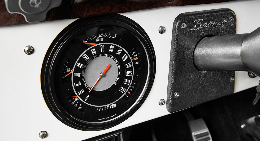 Classic Ford Bronco speedometer and tachometer on white dashboard with Bronco emblem plaque