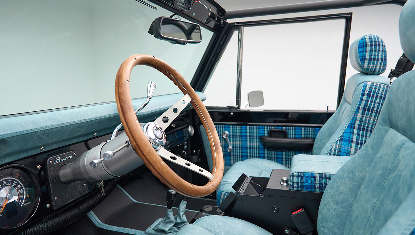 Classic Ford Bronco interior showing wooden steering wheel and blue plaid seats