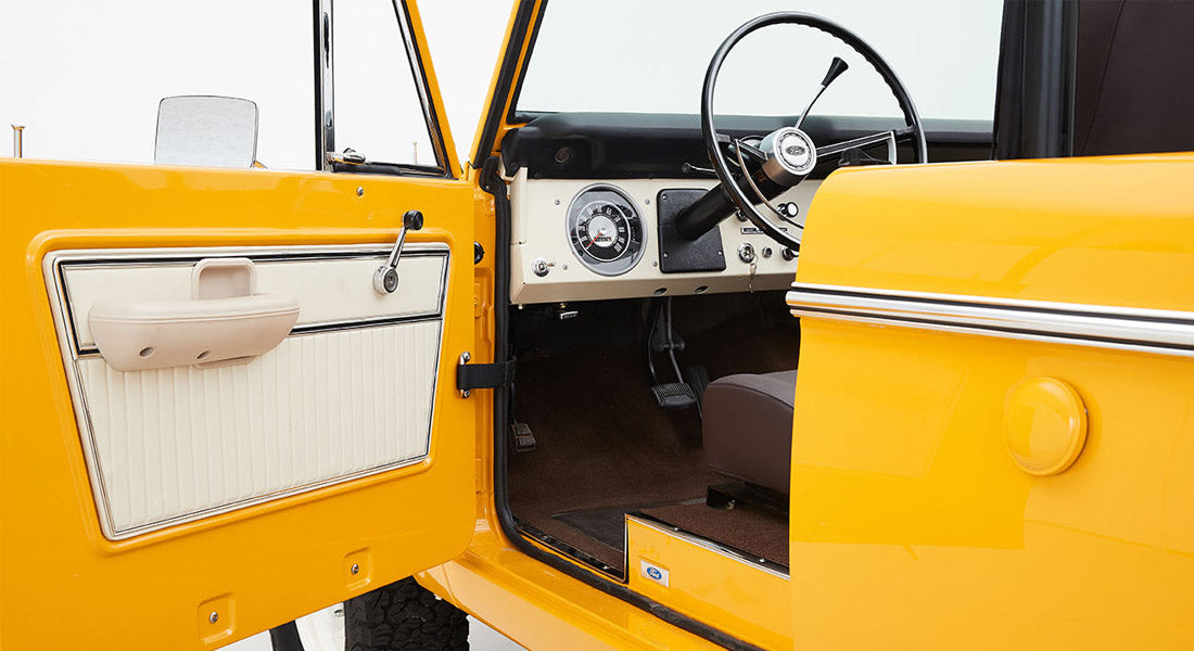Open yellow Classic Ford Bronco door showing cream and black interior door panel and steering wheel