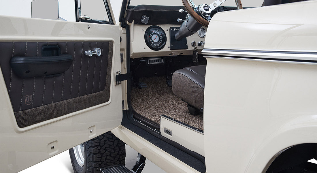 Open driver door revealing beige and brown interior door panel and part of Classic Ford Bronco dashboard