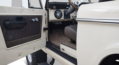 Open driver door revealing beige and brown interior door panel and part of Classic Ford Bronco dashboard