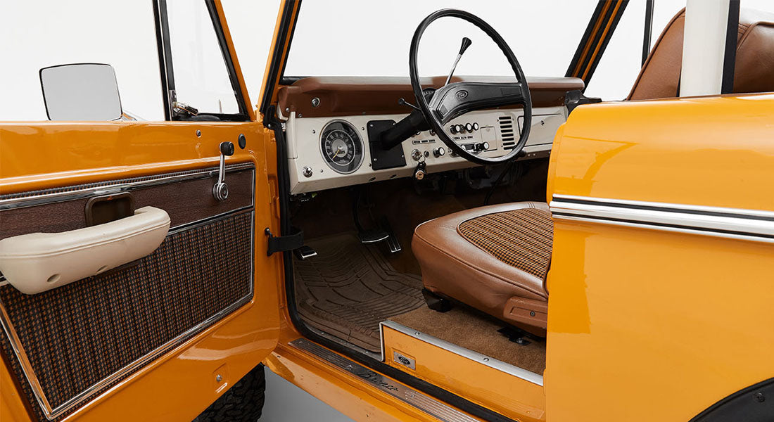 Open driver side door of a yellow Classic Ford Bronco showing interior door panel and seat