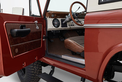 Open driver-side door showing vintage interior of a Classic Ford Bronco with steering wheel and dashboard.