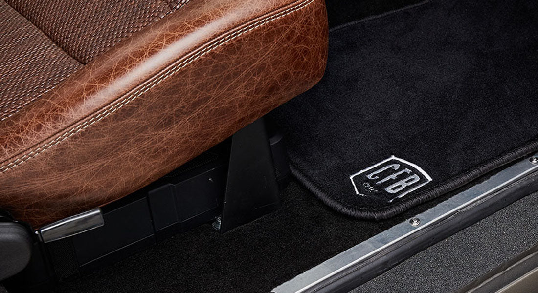 Black door mat with CFBI logo next to brown leather seat inside a Classic Ford Bronco