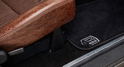 Black door mat with CFBI logo next to brown leather seat inside a Classic Ford Bronco