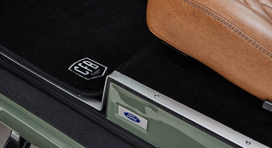 Black floor mats with white CFB Series logo and tan leather seat base in Classic Ford Bronco