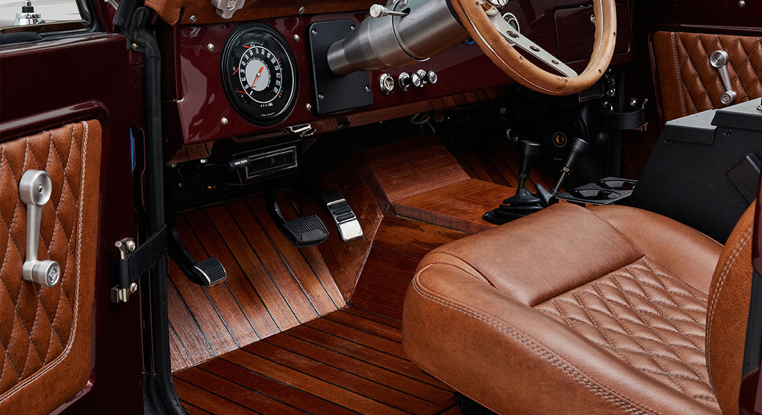 Inside view of Classic Ford Bronco cabin showing brown leather seats, wood trimmed floor, and dashboard with gauges