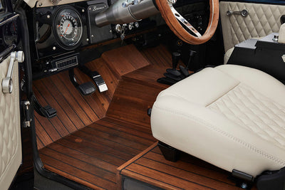 Classic Ford Bronco driver side floorboard with wood finish and beige seat with steering wheel visible