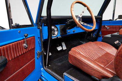 Interior of Classic Ford Bronco showing blue door, brown leather seat, and wooden steering wheel