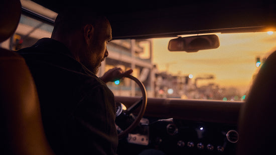 Man driving vehicle at sunset, visible from inside with dashboard and steering wheel