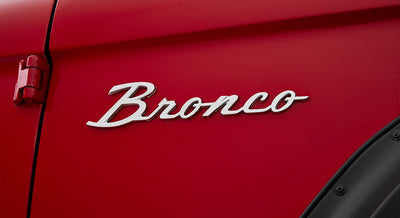 Chrome Classic Ford Bronco emblem on red vehicle door with visible door hinge