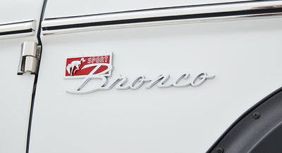 Close-up of white Classic Ford Bronco exterior with silver Bronco emblem and red background