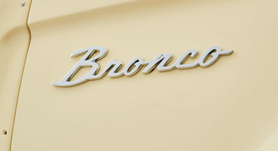 Chrome 'Bronco' emblem on the rear tailgate of a cream-colored Classic Ford Bronco