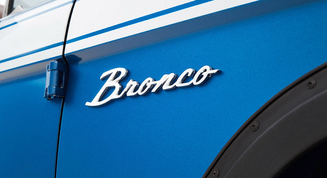Chrome Bronco emblem on blue vehicle exterior near door hinge and black fender trim
