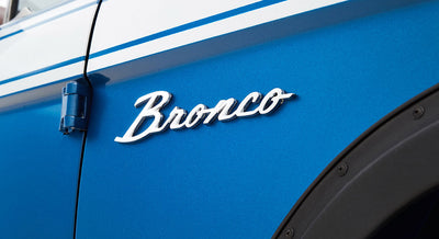 Chrome Bronco emblem on blue vehicle exterior near door hinge and black fender trim