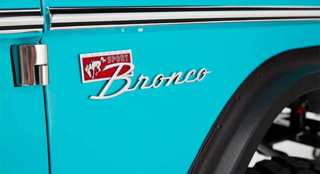 Classic Ford Bronco SPORT emblem on turquoise door panel next to silver hinge and black fender edge
