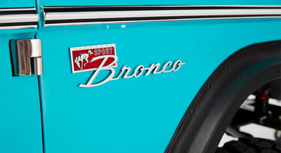 Classic Ford Bronco SPORT emblem on turquoise door panel next to silver hinge and black fender edge